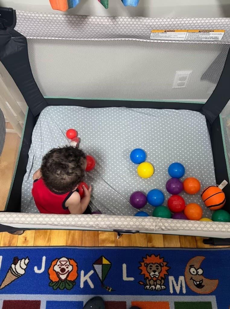 A toddler playing with colorful balls in a playpen