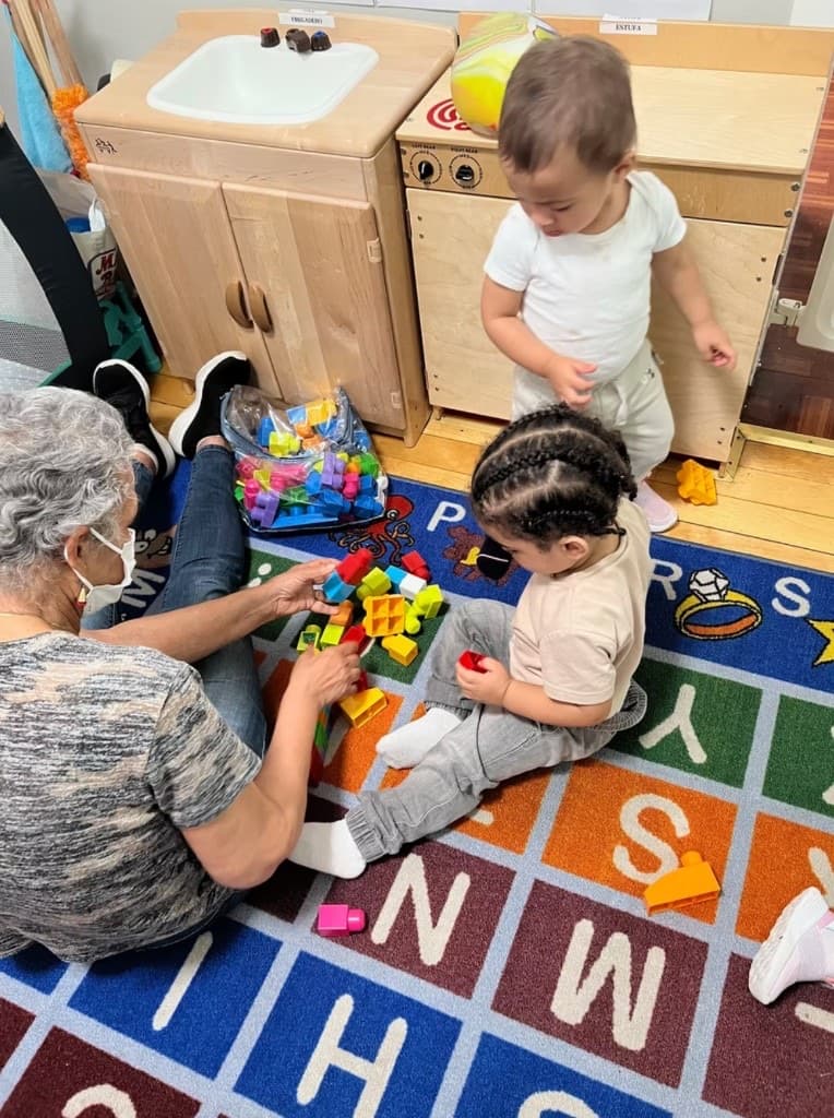 An educator and children playing with blocks on an alphabet rug