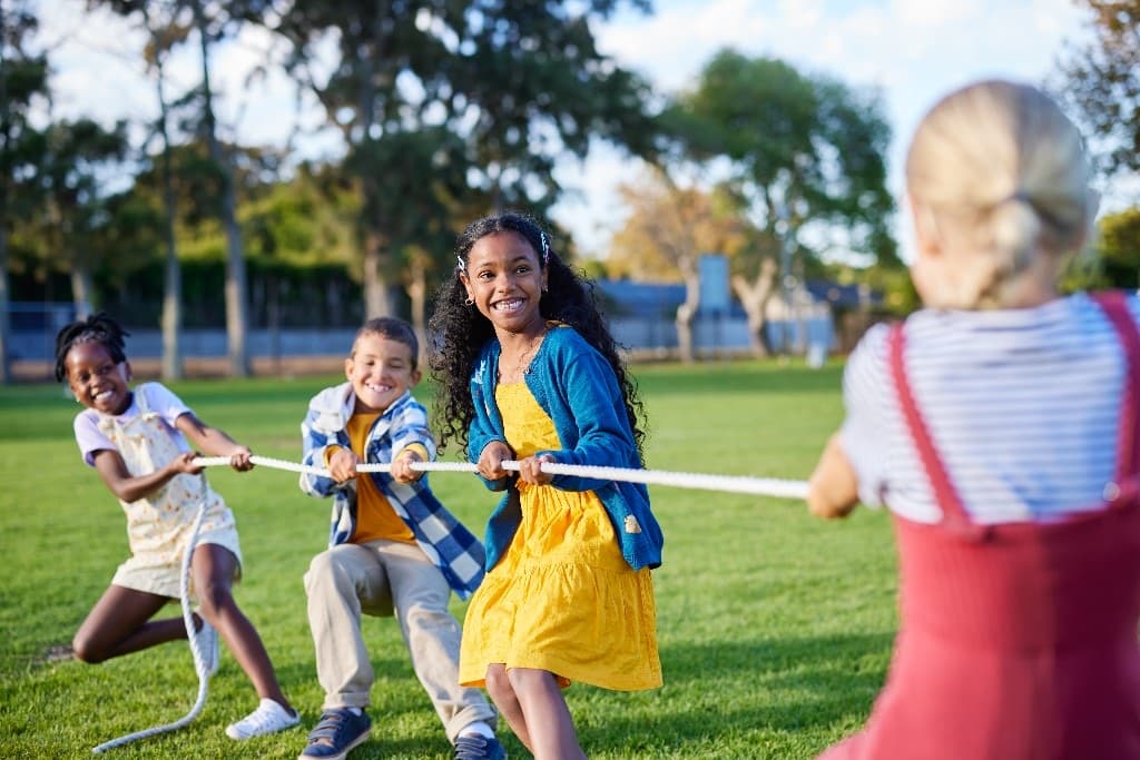 Children playing tug-of-war together on a sunny field
